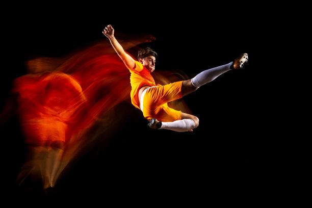 全身像的年轻人水平足球，足球运动员训练孤立在黑色背景。混合光图片下载