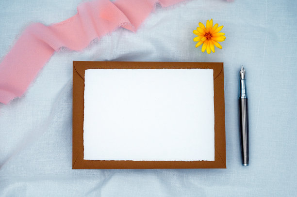 白色信纸，棕色信封，黄色金盏花，粉红色雪纺绸带，白色棉麻纱上的钢笔。图片下载