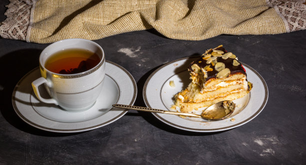 静物——分层的自制海绵蛋糕和一杯红茶放在白色的盘子里，亚麻餐巾，黑色的背景，强光，低调的照片。图片下载