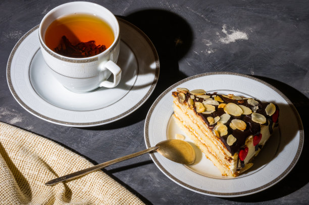 静物——分层的自制海绵蛋糕和一杯红茶放在白色的盘子里，亚麻餐巾，黑色的背景，强光，低调的照片。图片下载