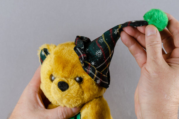 两只手拿着一个带着绿色巴拉邦帽的软玩具熊。一个男人图片下载