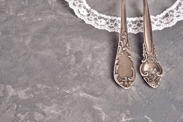 复古的餐具放在白色蕾丝餐巾上，背景是灰色的混凝土表面图片下载