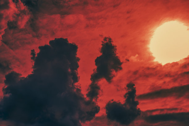 深红的落日映衬着大小不一、异想天开的黑色云层的轮廓。有选择性的重点。图片下载