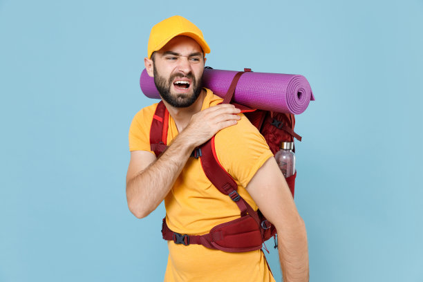 生病的旅行者年轻男子在黄色t恤帽背包孤立在蓝色背景。周末出游的游客。旅游发现徒步旅行的概念。感觉疼痛，痉挛，背部扭伤或颈部。图片下载