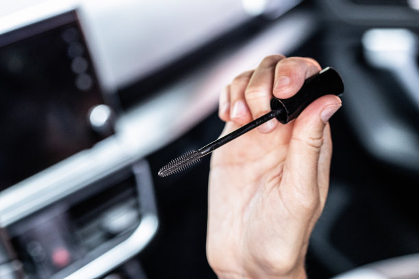 一个女人开车时手拿睫毛膏的近景。图片下载