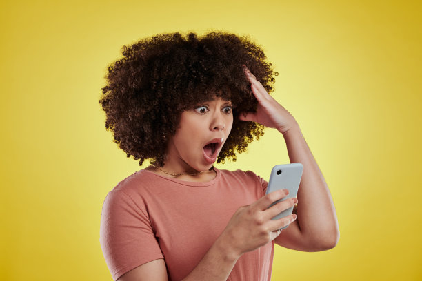 一名年轻漂亮的女子用智能手机拍摄，在黄色背景下看起来很震惊图片下载