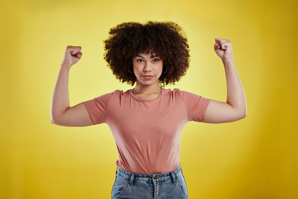 摄影棚拍摄的年轻女子弯曲她的二头肌在一个黄色的背景图片下载