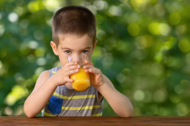 小男孩喝着玻璃杯里的橙汁图片下载