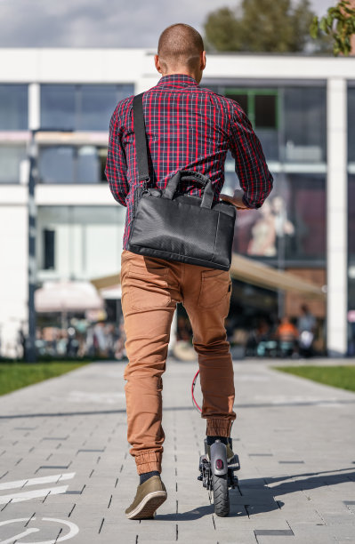 穿着休闲裤子和衬衫的年轻人骑着他的电动摩托车，从后面看过去，背景是建筑物图片下载