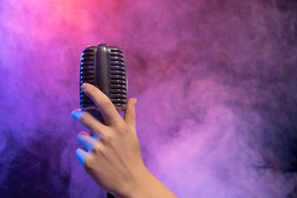 在霓虹灯和舞台烟雾中，舞台麦克风在女性手中被隔离的渐变蓝紫色背景。性能图片下载
