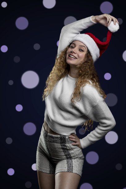欢快的拉丁女孩庆祝圣诞与圣诞老人的帽子和背景与散焦灯，文本空间。高质量的照片图片下载
