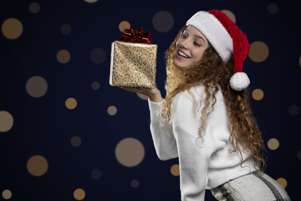 年轻的拉丁妇女展示圣诞礼物与圣诞老人的帽子。空间的文本图片下载