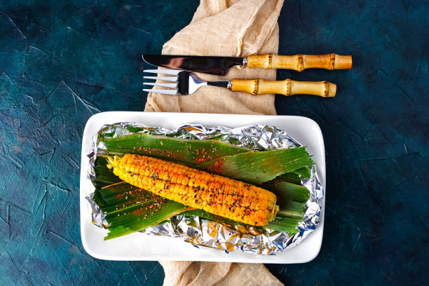 在篝火上烤玉米棒的一种方法，用香料烤甜玉米。烤蔬菜，素食餐。煮熟的玉米。图片下载