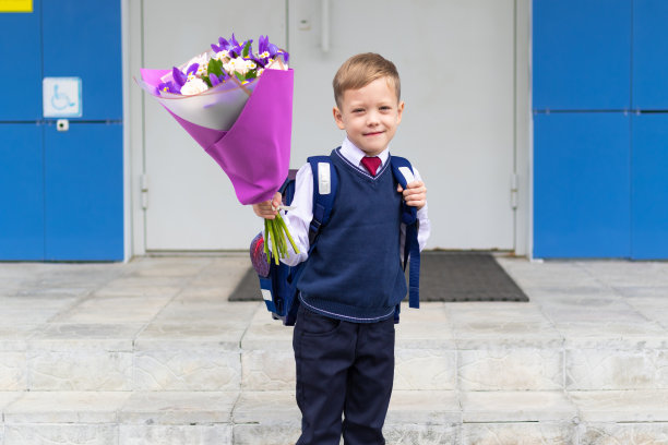 9月1日假期结束后，一名可爱的一年级男孩穿着校服，手捧一束五颜六色的鲜花在校园里。知识的一天图片下载