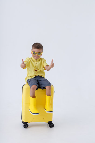 可爱的男孩坐在旅行袋上，竖起大拇指图片下载