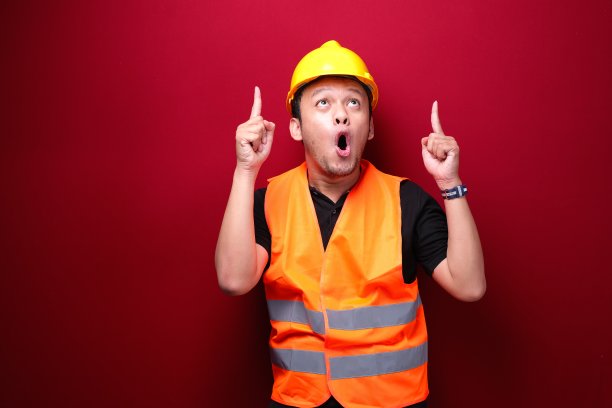 年轻的亚洲男工人很惊讶，用他孤立在红色背景上的手指着上面大喊哇。图片下载