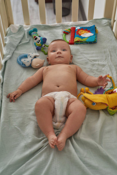 有趣的婴儿在尿布在婴儿床与发展玩具图片下载