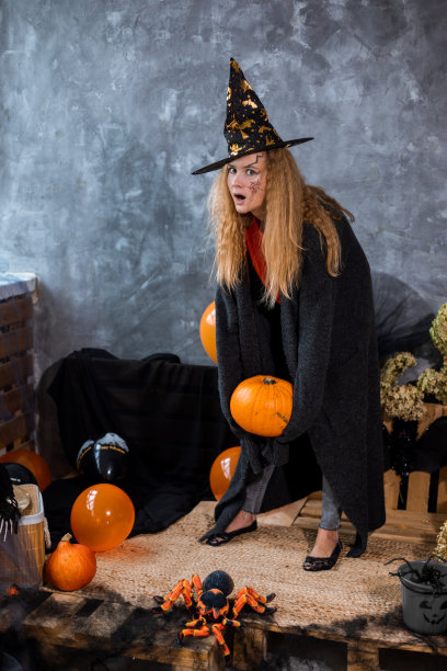 十几岁的女孩戴着帽子在装饰万圣节节日，手里拿着大南瓜。完整的照片图片下载