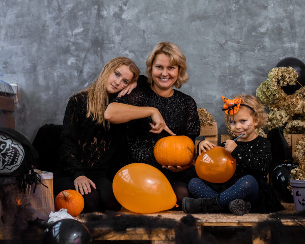妈妈和孩子两个女孩和女儿在装饰与橙色和黑色的色调万圣节有乐趣和花时间图片下载