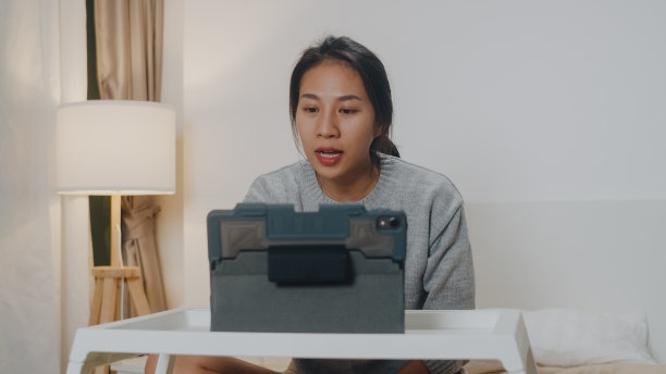 亚洲女商人使用平板电脑与同事进行视频通话，同时在卧室的床上智能工作。图片下载