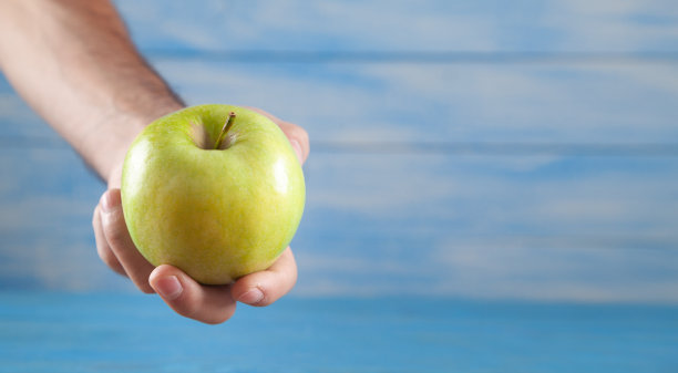 蓝色背景下，一名男子手握绿苹果。图片下载