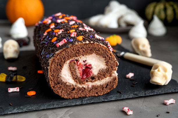 巧克力蛋糕卷与奶油和樱桃，装饰糖果万圣节在黑暗的混凝土背景。有选择性的重点。图片下载