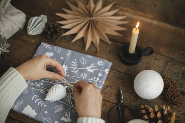 手用剪刀、手工纸星星、蜡烛在质朴的木桌上用织物包装圣诞礼物。大气多变的时光，北欧风情。圣诞快乐，节日快乐!“零浪费”图片下载