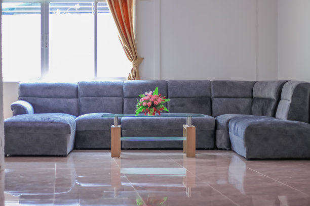 时尚的客厅内部与玫瑰花瓶玻璃桌子，时尚的沙发家具和阳光，金色窗帘在窗口的家庭背景图片下载