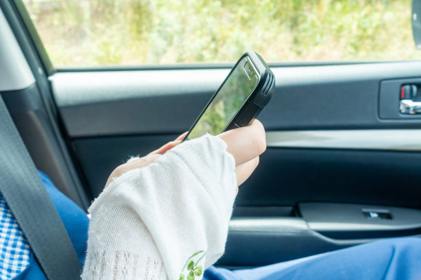 一名女子坐在汽车的副驾驶座位上看智能手机。智能手机成瘾的形象。图片下载
