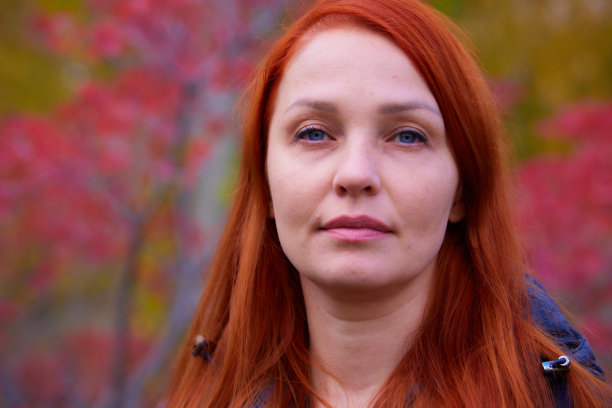 一个生活风格的女人的肖像与红色的头发在秋天的背景下五颜六色的树叶图片下载