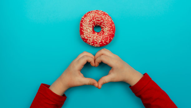 这是食物创造的完美理念。一张美味的甜甜圈的照片，上面有五颜六色的水花和两只婴儿的手图片下载