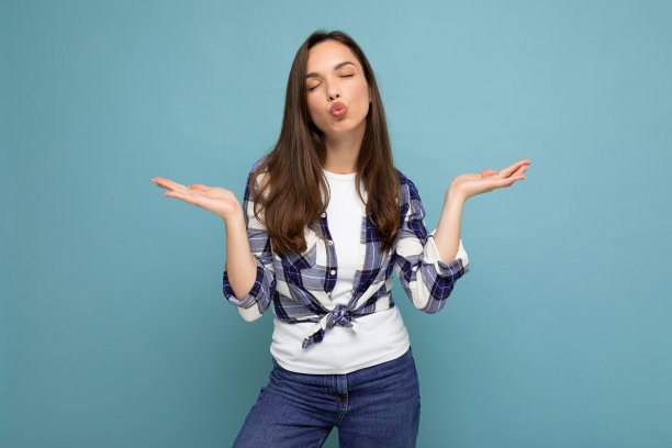 年轻的积极快乐美丽的winsom黑发女人与真诚的情感穿着格子衬衫在蓝色背景与副本空间保持孤立的双手，并给予亲吻图片下载
