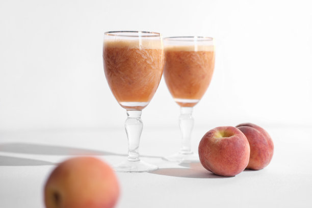 玻璃杯里的桃子冰沙，白色背景上有三个桃子。健康的维生素补充饮料和夏季营养餐。图片下载