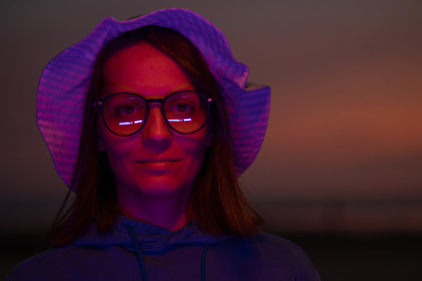 一位欧洲妇女戴着一顶帽子，在夕阳的天空背景下被霓虹灯照亮图片下载