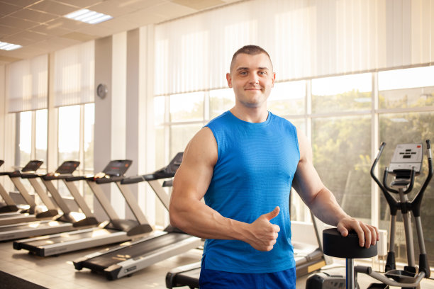 一个年轻英俊的教练，肌肉发达的身体在健身房摆姿势。健美，运动理疗，减肥。运动是一种很酷、健康、积极的生活方式。室内概念。图片下载