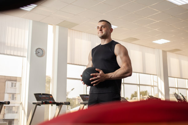 肌肉教练在蹦床上投球，肌肉教练，健身房。一个漂亮男人的肖像，教练，个人减肥和体育课程。图片下载