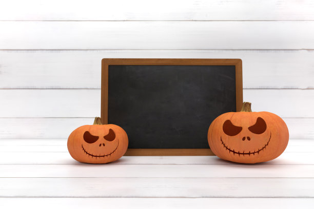 两个令人毛骨悚然的万圣节南瓜，Jack O灯笼，白色木头背景上有一张邪恶的脸和眼睛和黑板。图片下载