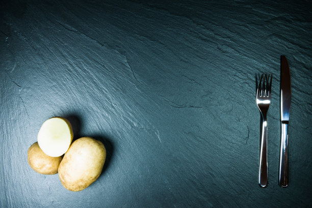 黑色花岗岩拖鞋。黄色的土豆和刀叉。工作室的照片。图片下载