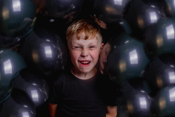 可爱有趣的欧洲小男孩被黑色气球包围着。脸特写。那男孩生气了，龇牙咧嘴。背景的气球。图片下载
