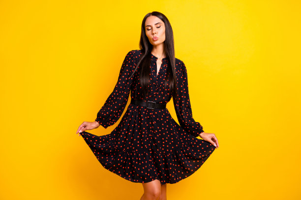 照片中轻浮可爱的年轻女士穿着黑色衣服胳膊裙子送吻孤立的黄色背景图片下载