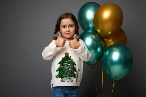 可爱可爱微笑的4岁小女孩穿着白色毛衣，竖起大拇指，看着相机，在灰色背景上与圣诞节和新年广告的复制空间隔离图片下载
