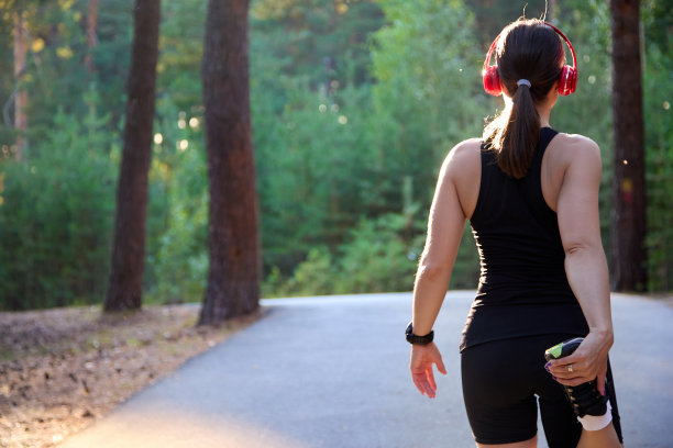 跑步运动员伸展双腿和双脚，准备在森林的柏油路上跑步。图片下载