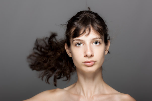 美丽的年轻女孩画室肖像在灰色的背景。看相机。多风的头发。图片下载