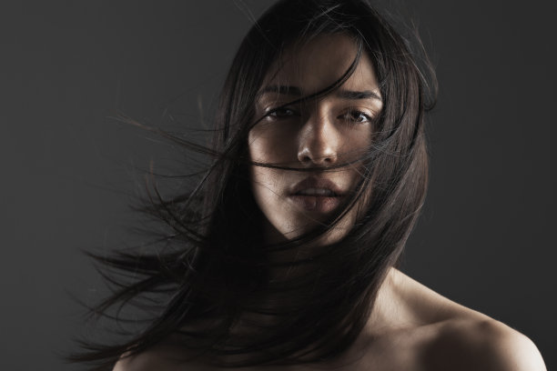 美丽时尚工作室的一个美丽的年轻女孩的肖像与风的头发在她的脸。图片下载