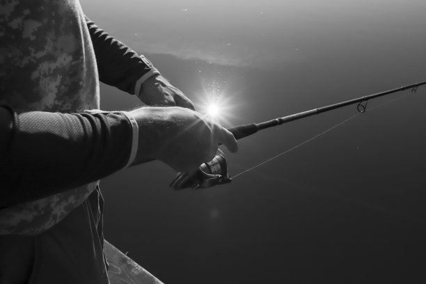 手握鱼竿近距离观看湖面反射的阳光，黑白照片图片下载