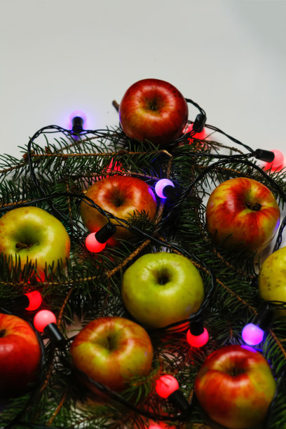 许多红色和黄色的有机苹果在节日圣诞树的背景与灯泡灯。食物和饮食。健康的水果背景。维生素成分。白色背景。垂直图片下载