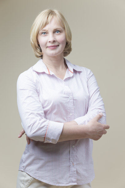 微笑的高加索成熟女人的肖像看着直与双手叠在米色背景。垂直的图像图片下载