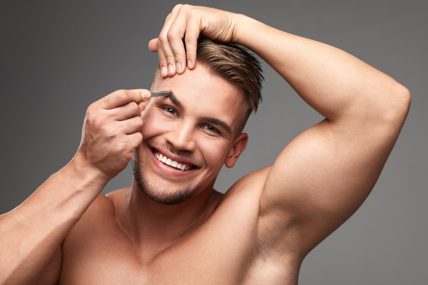 摄影室拍摄的一个英俊的年轻人拔他的眉毛在灰色的背景图片下载