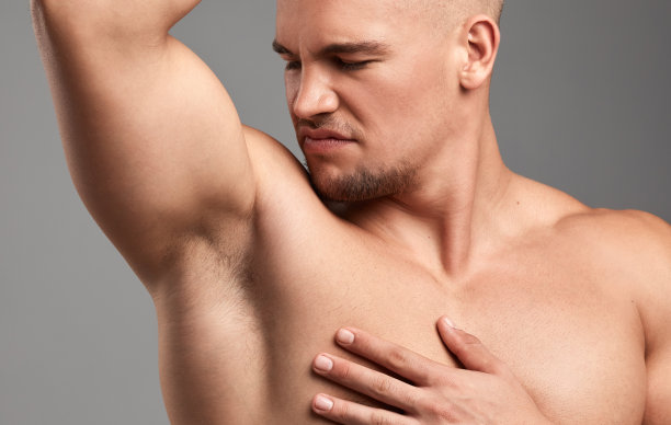 摄影棚里，一个英俊的年轻人在灰色的背景下闻他的腋窝图片下载