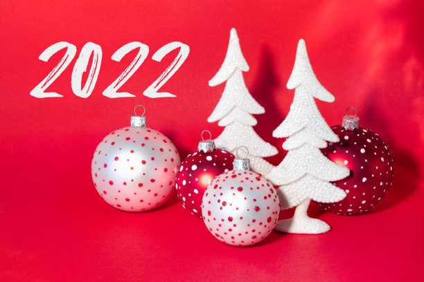 圣诞卡上有白雪覆盖的白色新年树和鲜红色背景上五颜六色的球。图片下载